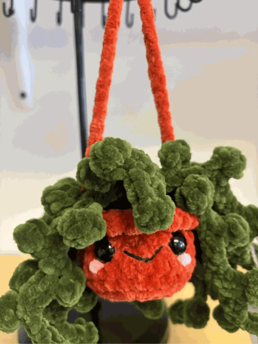 A charming handmade hanging plant string of pearls with orange and green crocheted pot and fluffy leaves