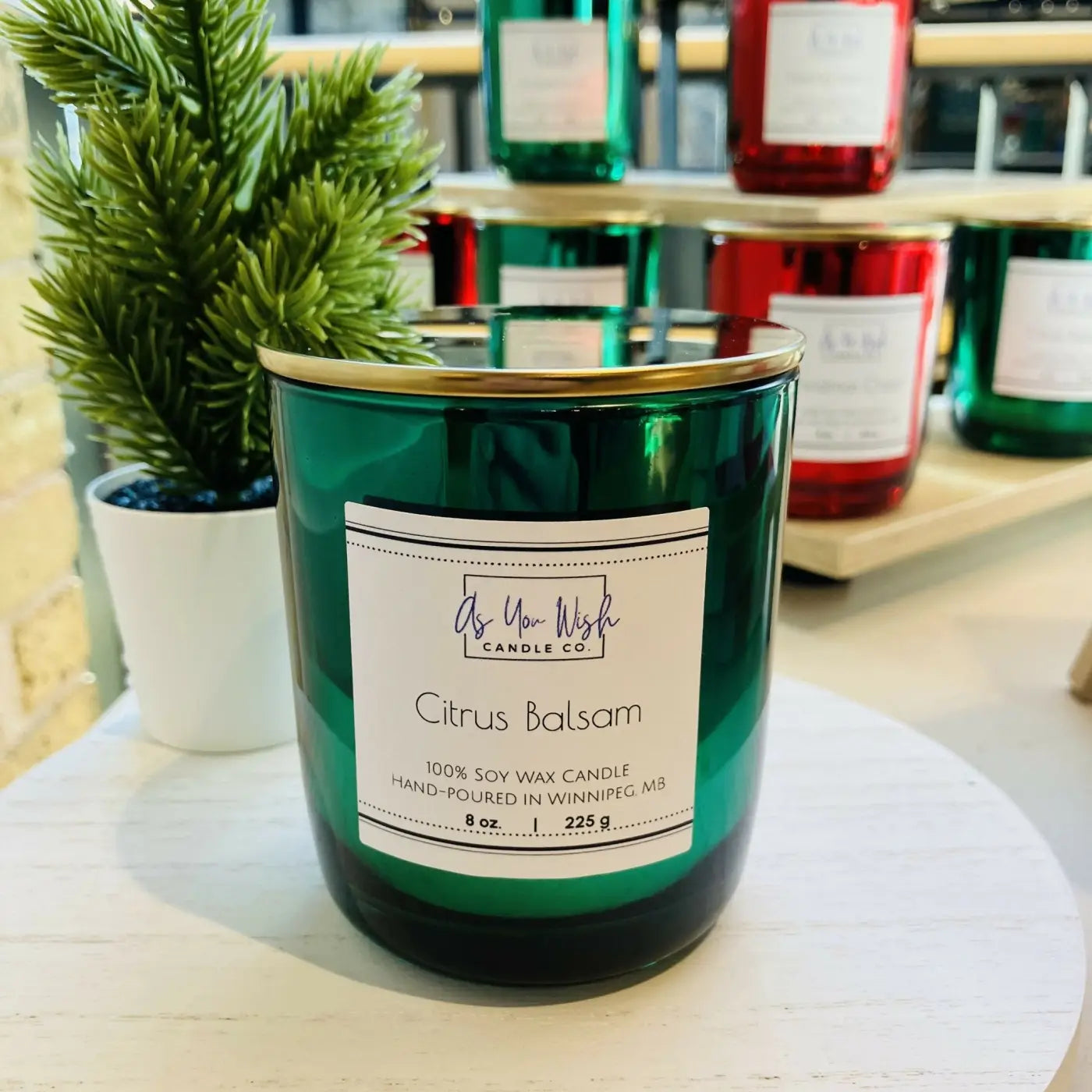 Emerald green glass wax candle jar with gold rim and white label featuring holiday luxury soy citrus balsam scent