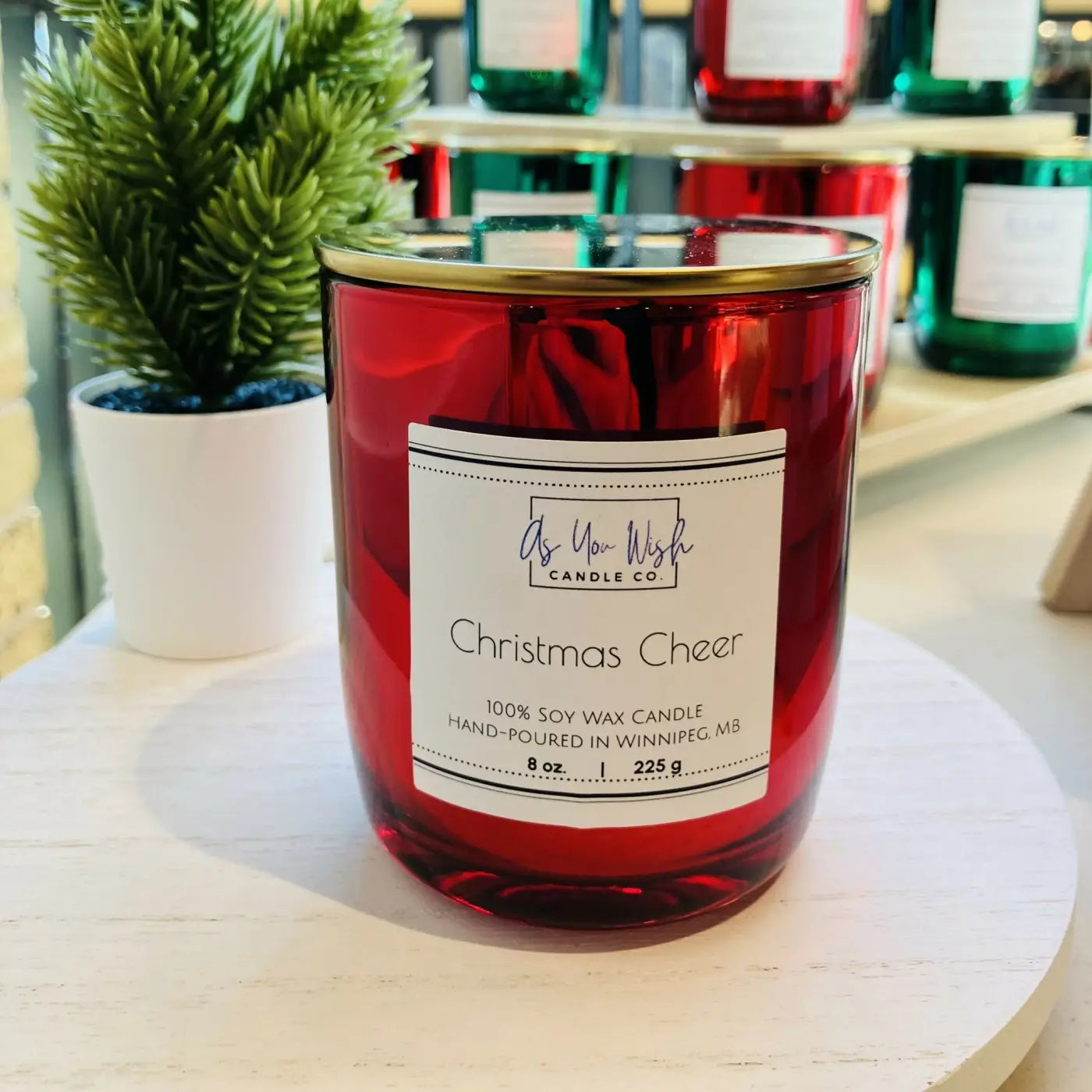 A vibrant red luxury soy wax candle jar with a gold lid and christmas cheer scent from as you wish candle co holiday luxury soy