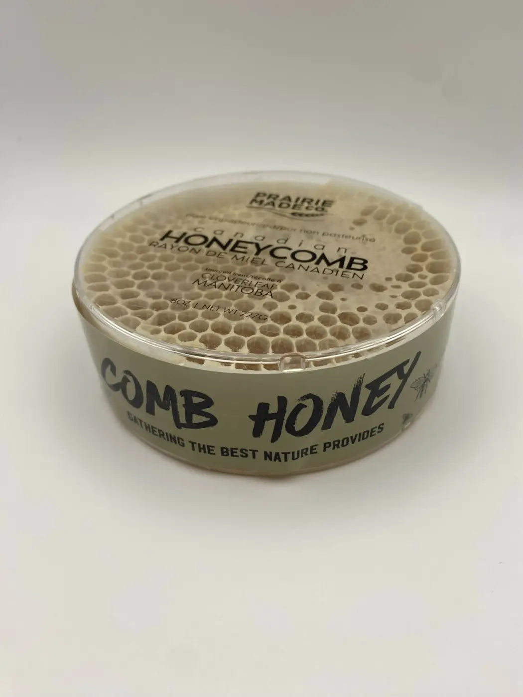 A clear round plastic container of prairie mades honeycomb with a honeycomb-patterned lid and beige label locally sourced