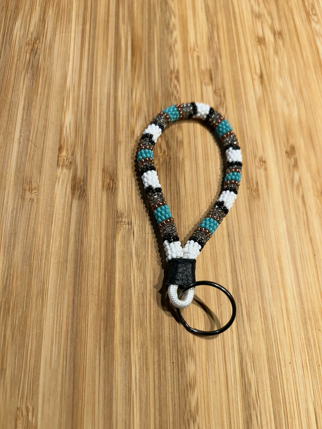 HERA Beaded Mini Keychain with leather and key ring on wood background.