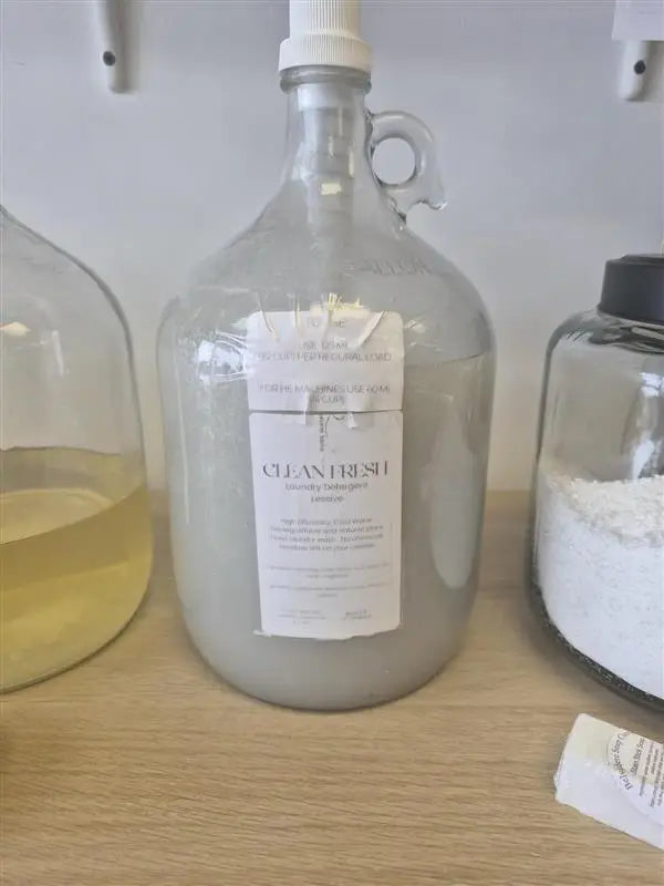 Clear glass jug with white pump labeled clean fresh laundry detergent for effective laundry use