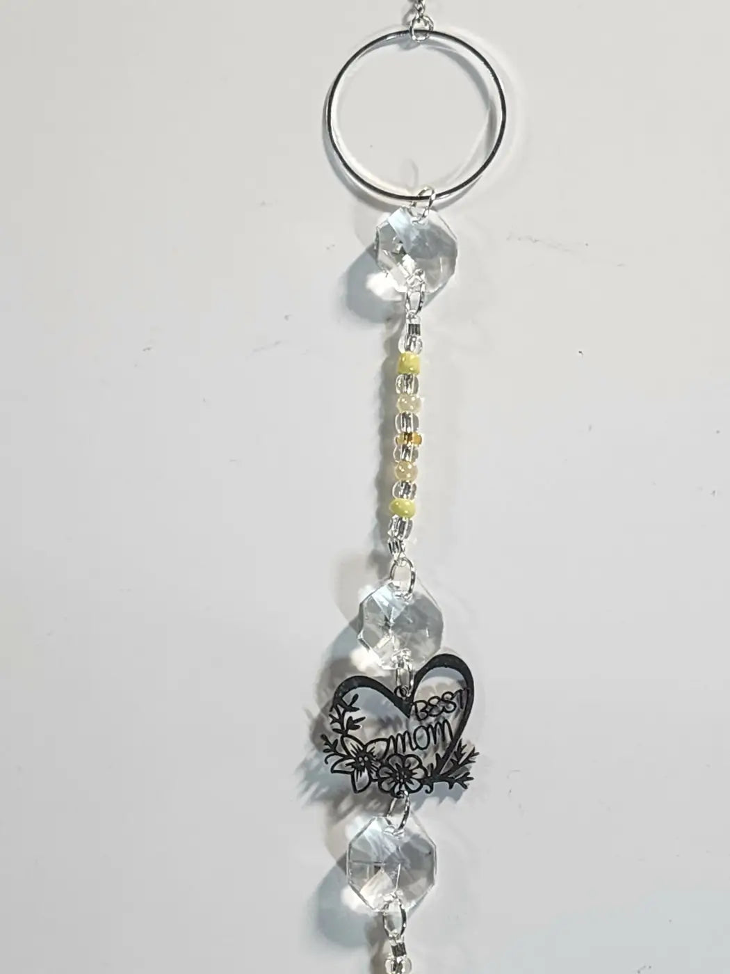 A clear crystal sun catcher with a black heart charm engraved sweet mom adorned with yellow and silver beads hanging from a ring