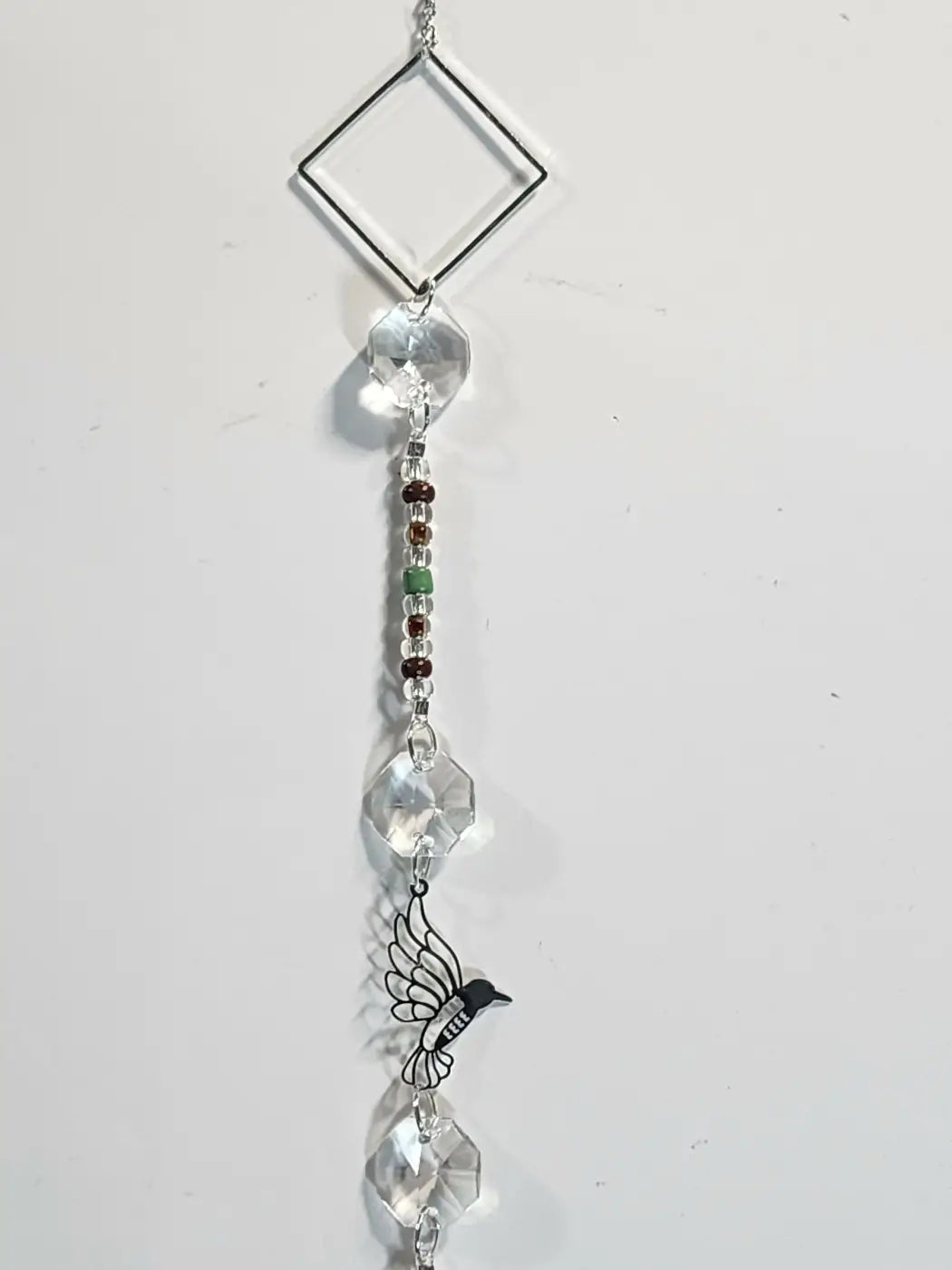 Long 9 features a delicate silver-toned diamond frame with clear crystal beads and a black hummingbird charm, ideal near direct sunlight