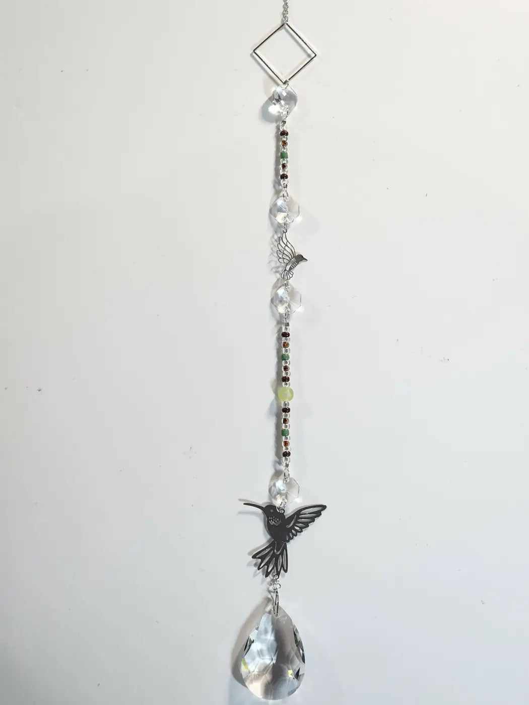 Delicate long suncatcher with clear crystal beads and black hummingbird charm hangs in direct sunlight, handmade soap canada style