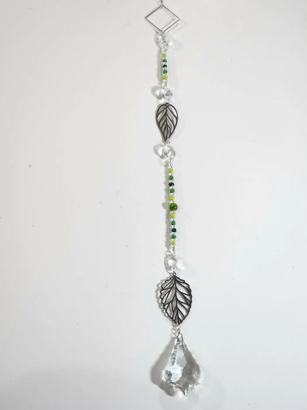 Long suncatcher with silver toned metal leaves, clear and green beads, and a crystal teardrop for direct sunlight decor