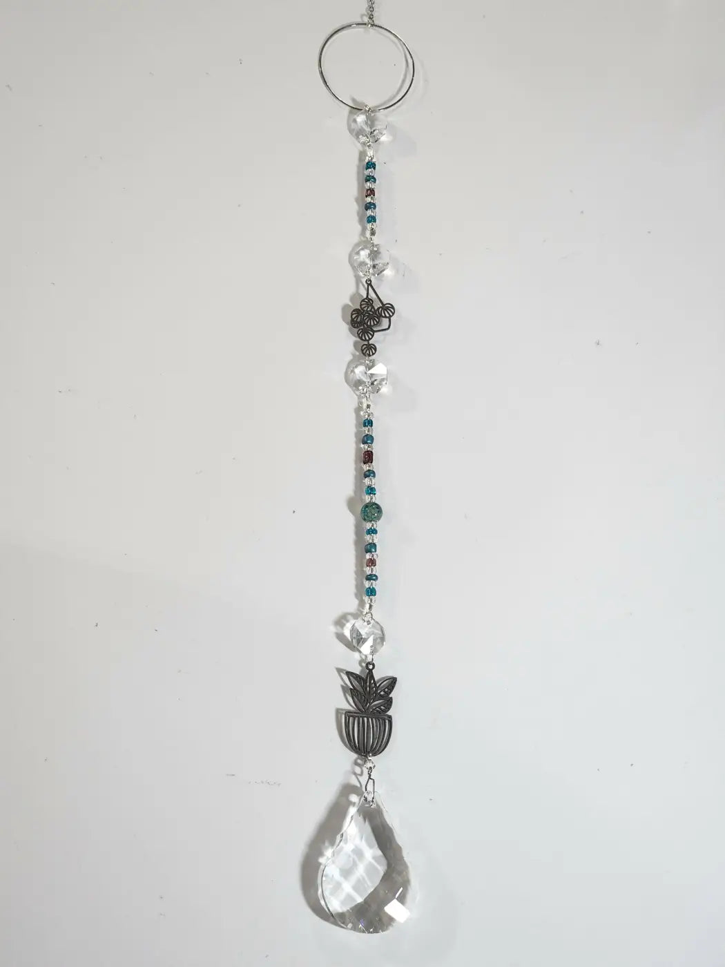 A long suncatcher with faceted teal and brown crystals and a silver ring designed for direct sunlight display