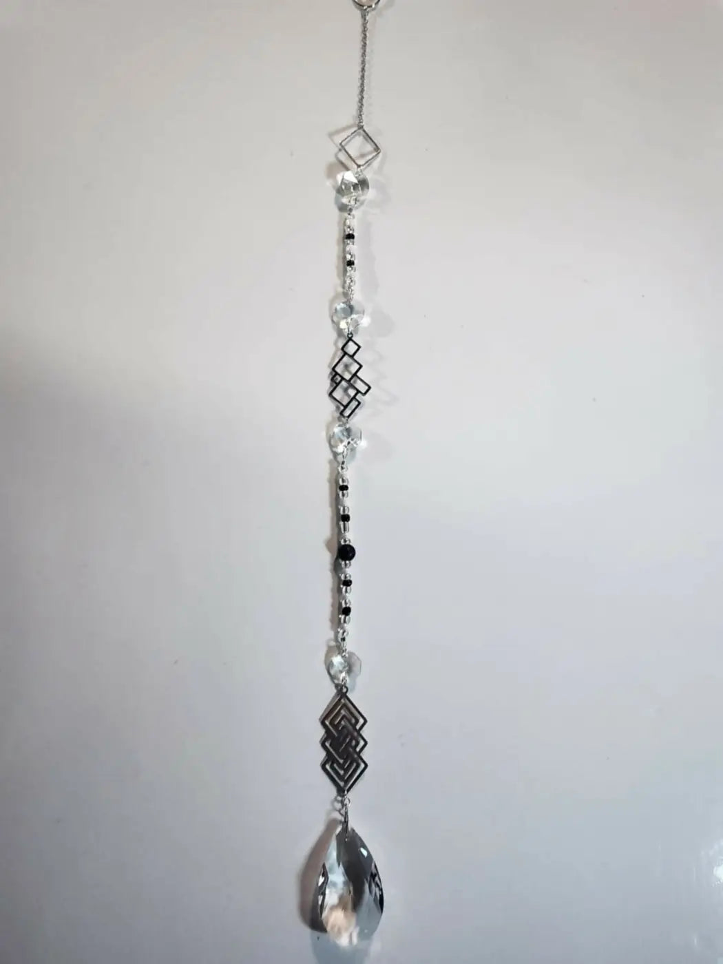 Long suncatcher with black and clear crystal diamond charms and teardrop prism hangs from silver chain in direct sunlight