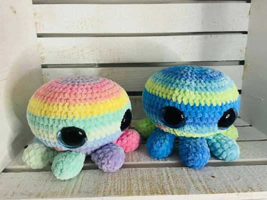 Two handmade mama octo crocheted octopus plush toys in pastel rainbow and blue green shades with large black eyes