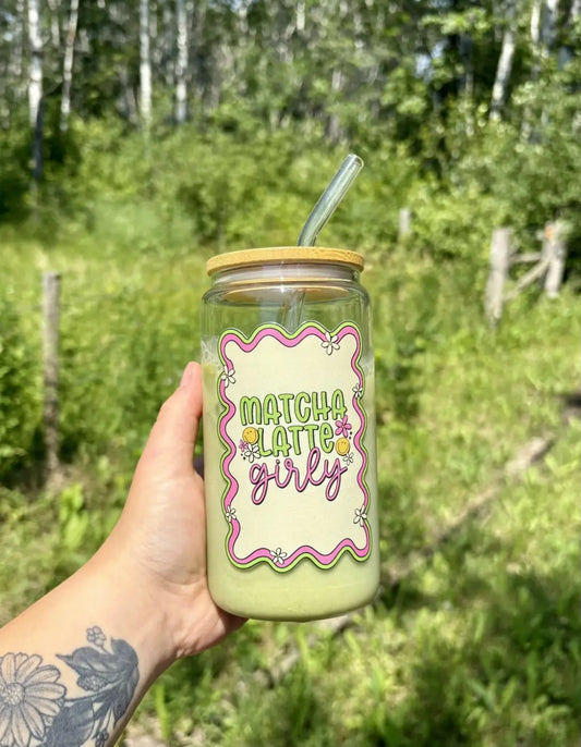 A clear matcha latte glass with wooden lid and straw featuring a green and pink decorative label pure wash design