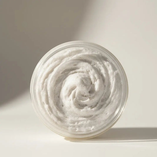 A clear glass jar of rocky mountain soaps men’s shaving cream whipped soap with creamy white scrub and dark granules