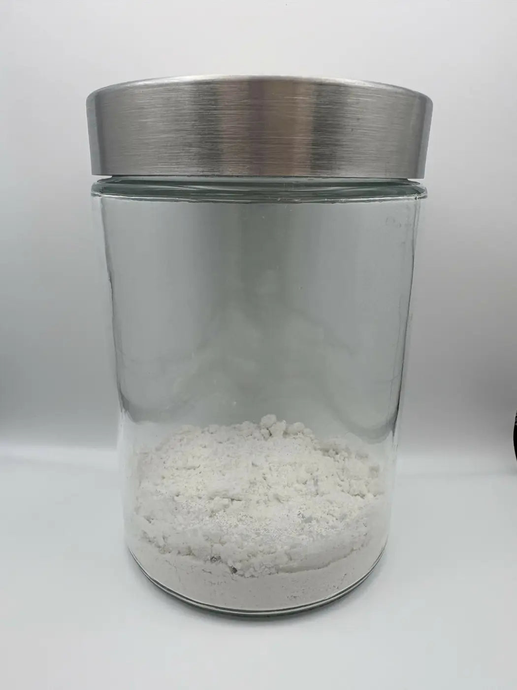 Clear glass jar with brushed stainless steel lid containing white granular mint toothpaste powder for dental care