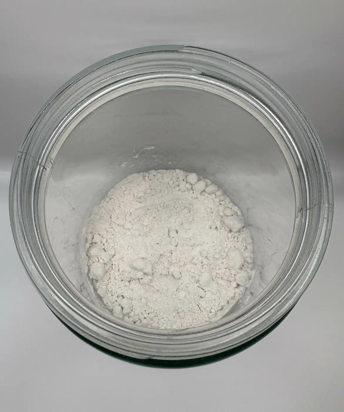 A clear glass jar filled with fine white powder of mint toothpaste powder for natural oral care use