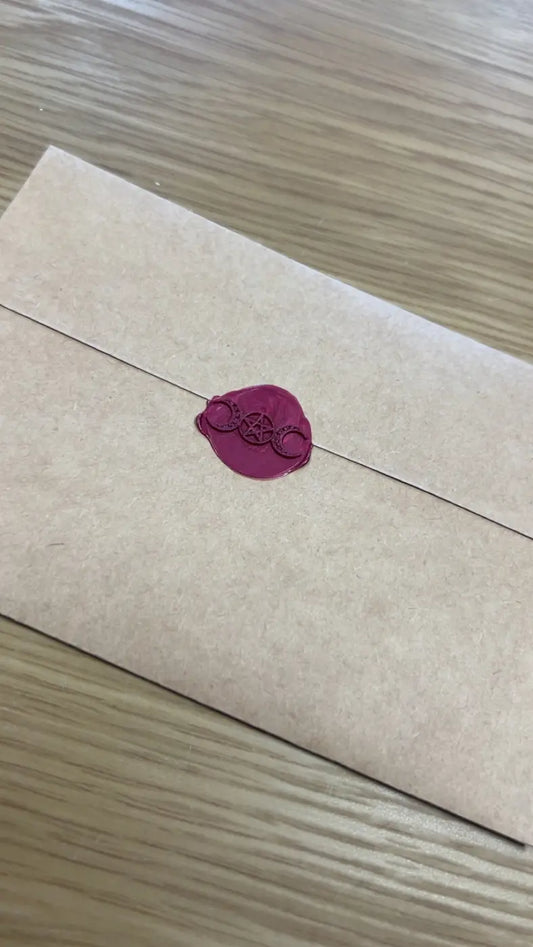 A matte beige envelope sealed with a magenta wax seal featuring an intricate design for a mystery tarot card