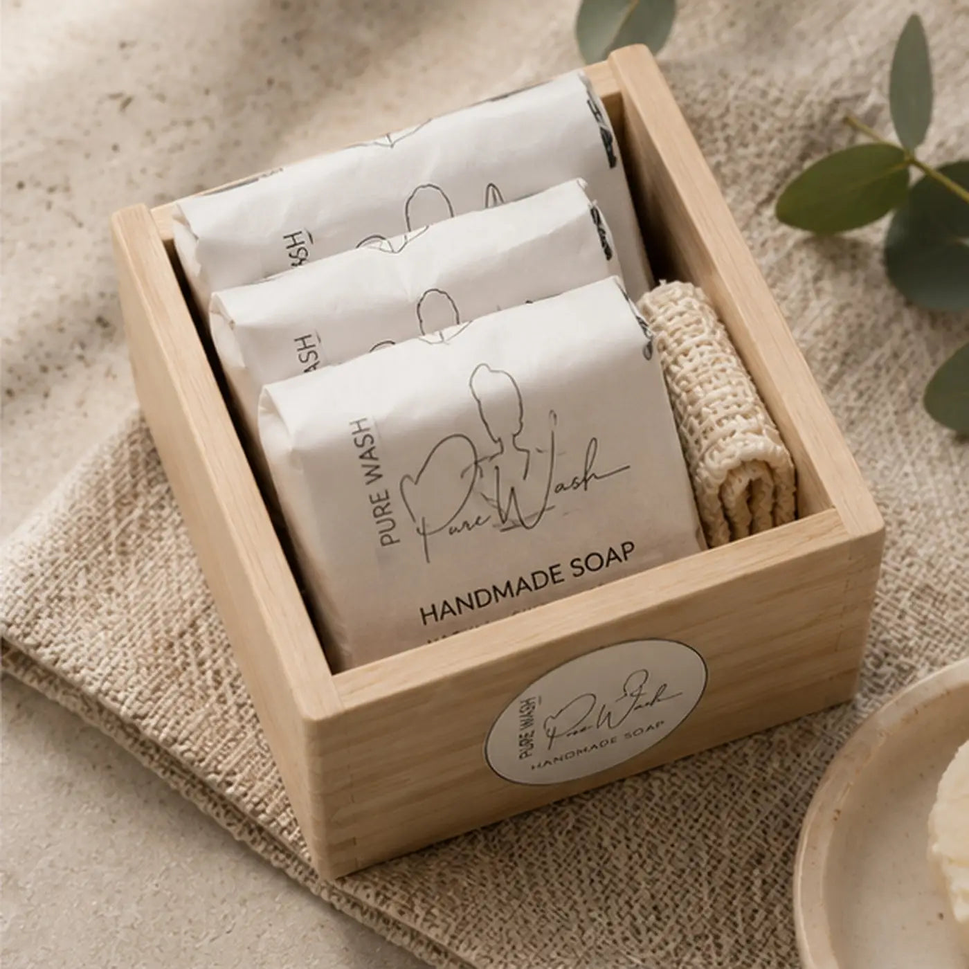 Light wood box soap containing three wrapped handmade soap bars and a woven sponge in a natural soap gift set