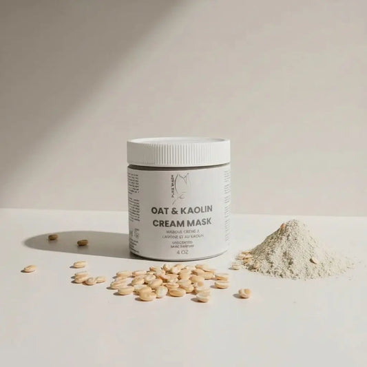White cylindrical jar of oat and kaolin cream mask with white lid surrounded by colloidal oatmeal and kaolin clay powder
