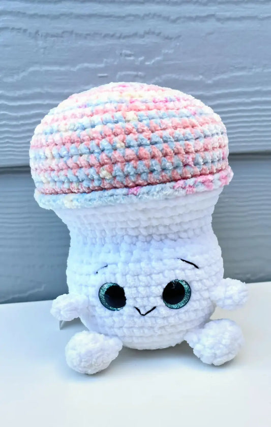 A charming pastel mushroom white crocheted plush toy with striped pink blue cap and glittery teal eyes for natural skincare canada
