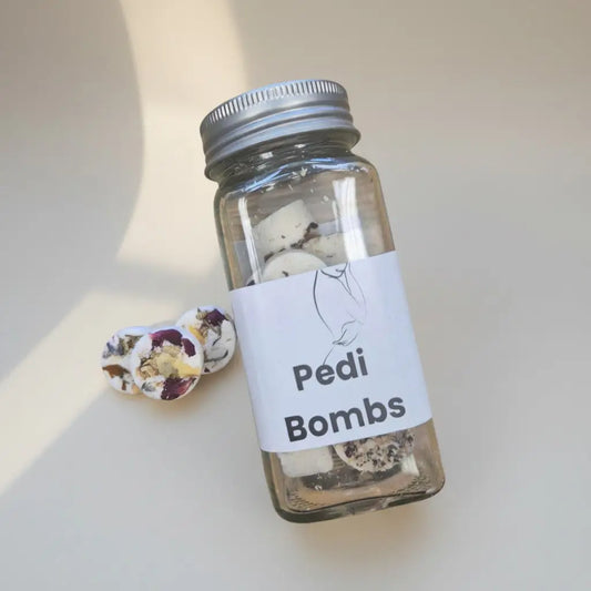 Clear glass jar with silver metal lid labeled pedi bombs featuring minimalist feet drawing for handmade soap Canada