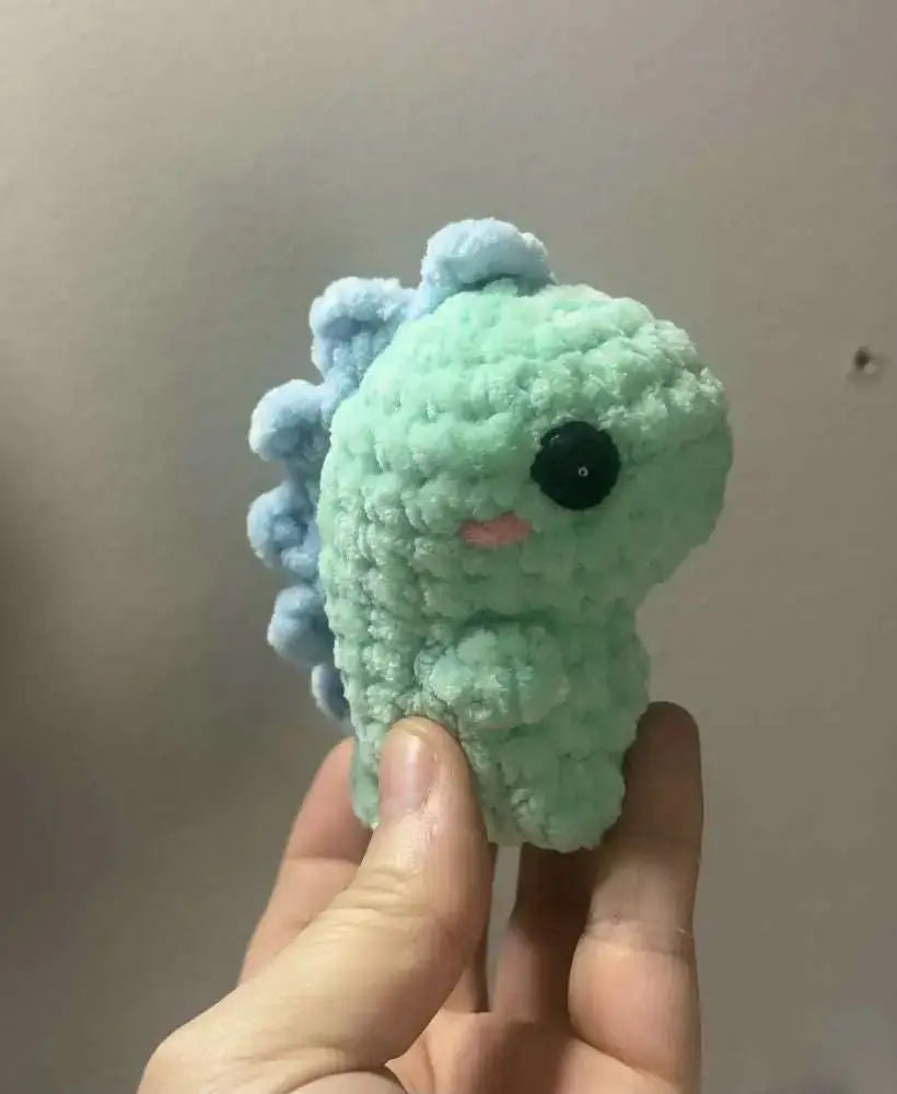 A soft mint-green crocheted pocket dinos dinosaur with light blue spines and black button eye, ideal for handmade soap canada