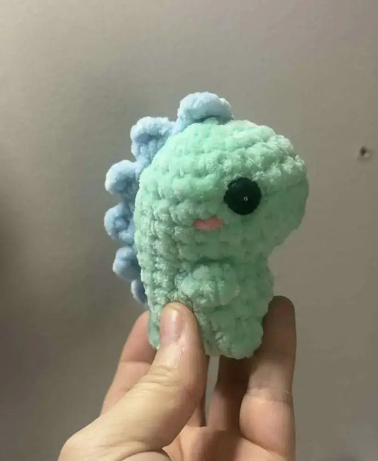 A soft mint-green crocheted pocket dinos dinosaur with light blue spines and black button eye, ideal for handmade soap canada