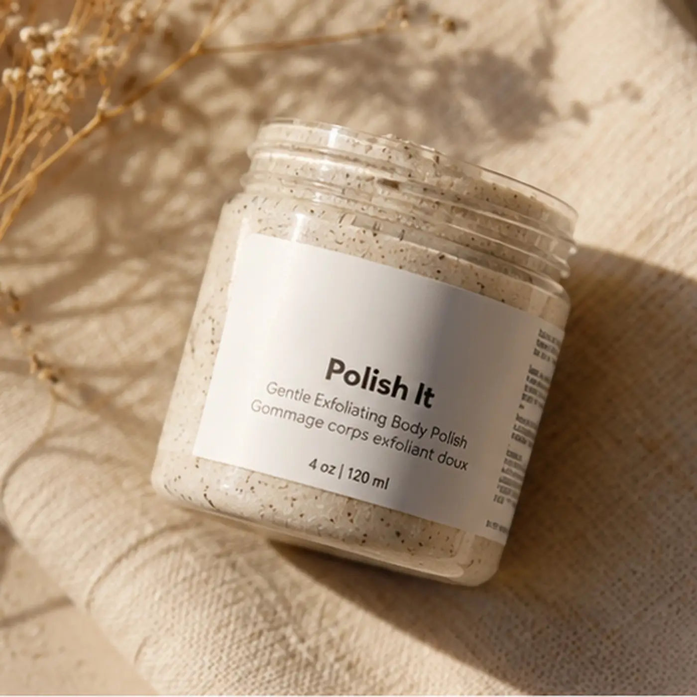 Clear glass jar of creamy exfoliant polish it with speckled beige granules for gentle dead skin removal and cucumber seed oil benefits