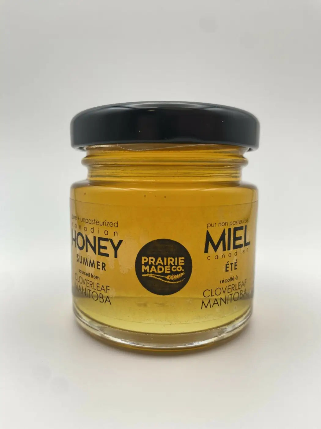 A clear glass jar of golden summer honey from prairie made co labeled cloverleaf manitoba in prairie made season honey sampler