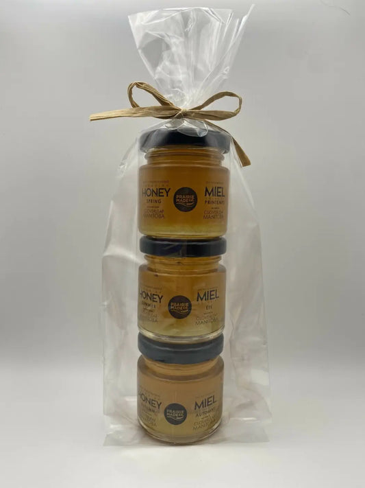 Three stacked glass jars of golden honey in the prairie made season honey sampler sealed with black lids and tied with twine