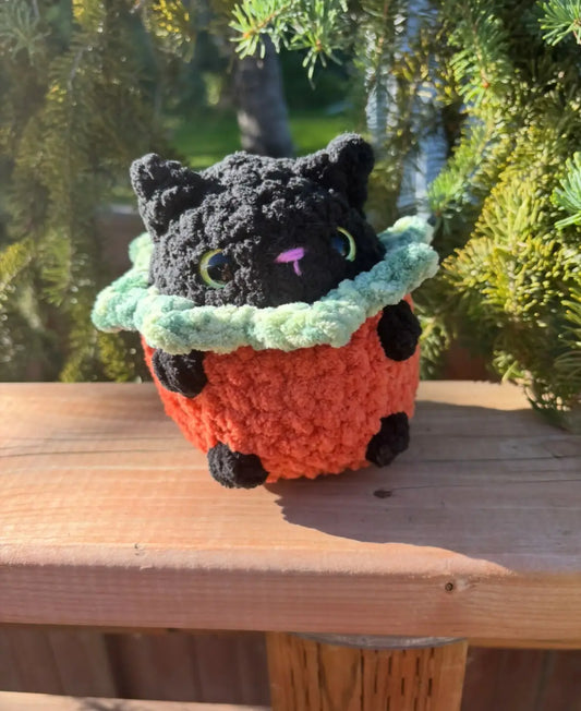 A handmade crocheted black cat with green eyes in an orange pumpkin cat crochet pot natural skincare canada
