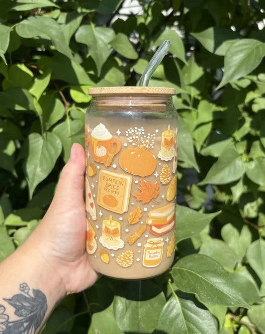 A clear pumpkin spice glass cup with orange pumpkin illustrations, bamboo lid, and green straw for autumn drinks
