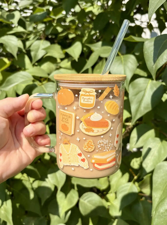 A glass pumpkin spice mug with a bamboo lid and handle featuring autumn-themed orange and beige illustrations