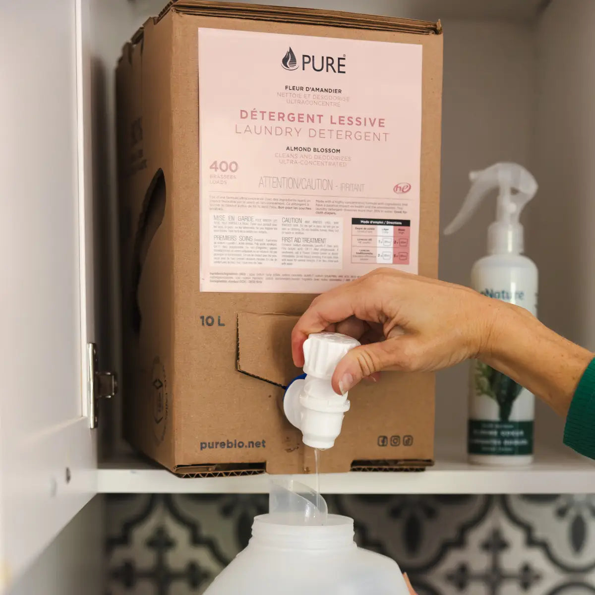 A white plastic dispenser with spout and knob attached to a cardboard box labeled pure laundry detergent refill instore