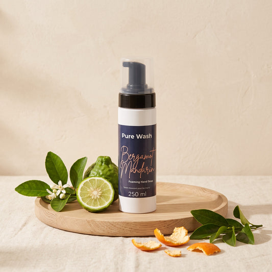 Pure Wash Bergamot Mandarin foaming hand soap in a white bottle on a wooden tray with fresh citrus fruit and leaves.