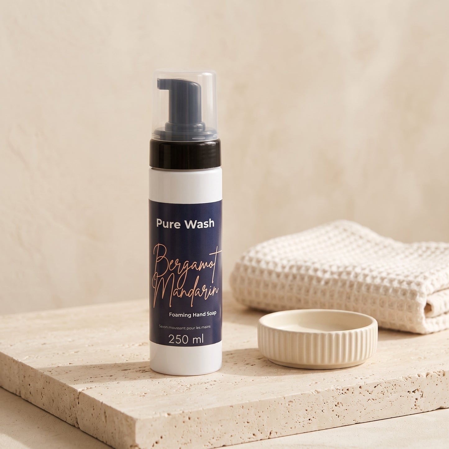 Pure Wash Bergamot Mandarin foaming hand soap in a white bottle with a pump on a textured stone surface with a towel.