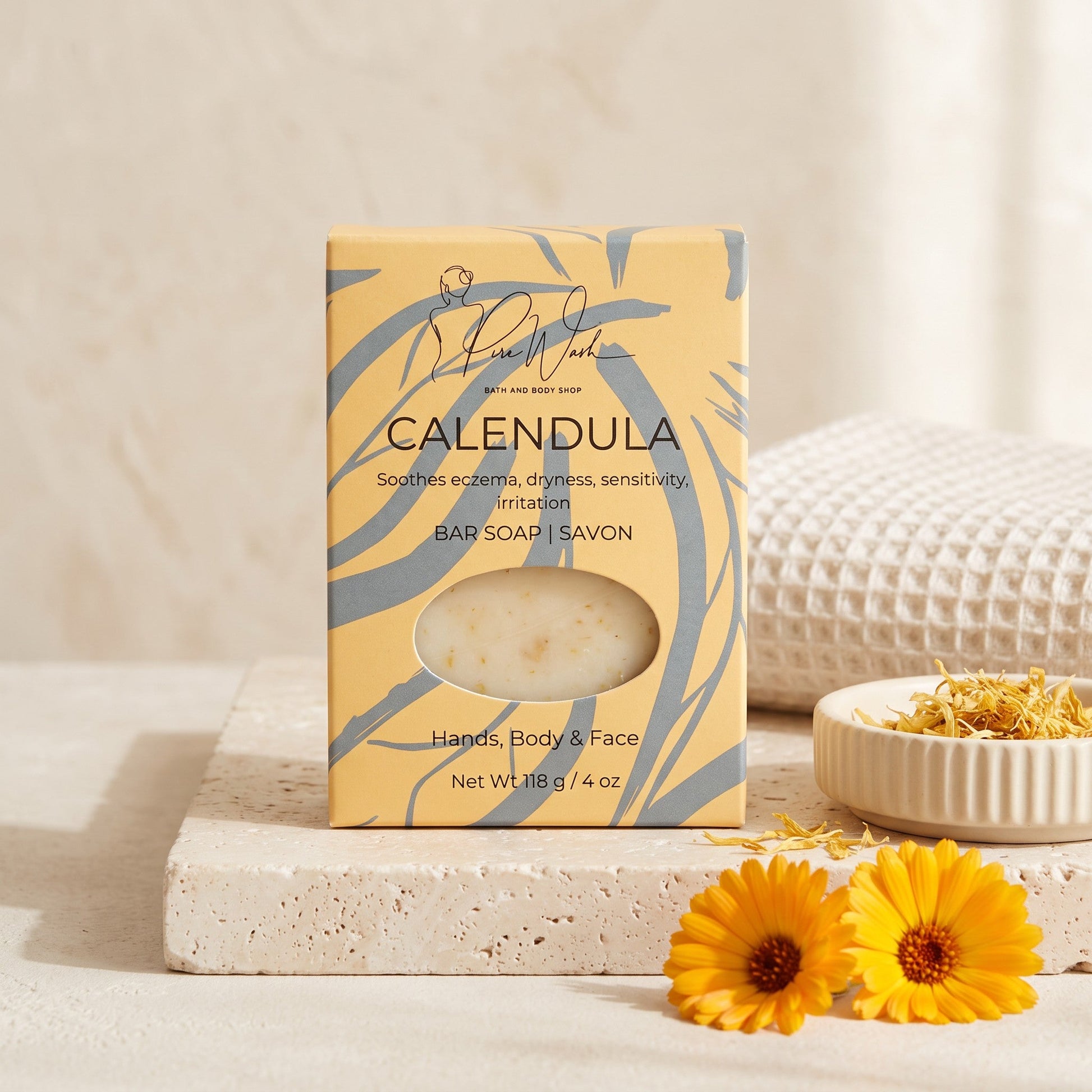 Pure Wash Calendula soap bar in yellow packaging with dried petals, on a stone tray with fresh calendula flowers.