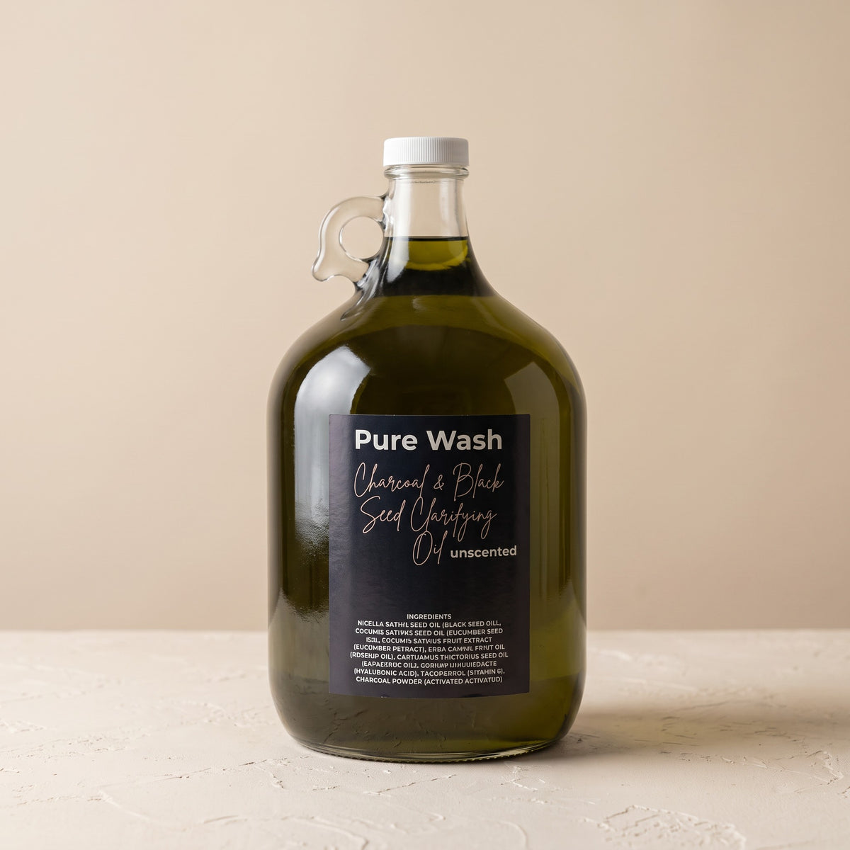 Pure Wash charcoal and black seed clarifying oil in a large glass refill jug for oily and blemish-prone skin