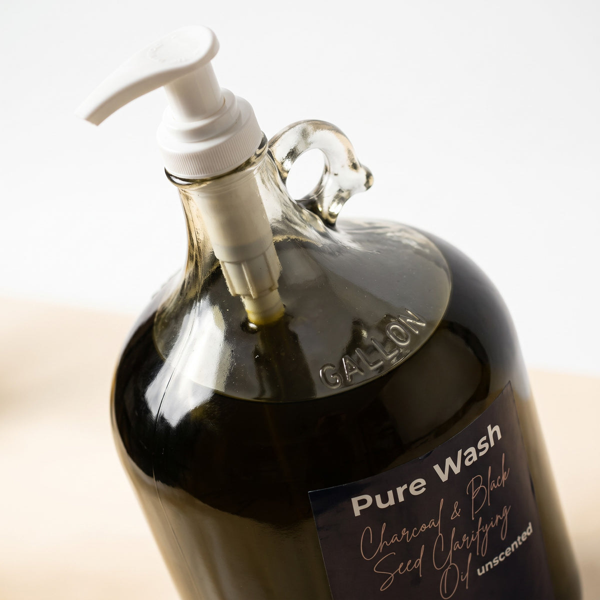 Pure Wash charcoal and black seed clarifying oil in a large glass gallon jug with a white pump dispenser.
