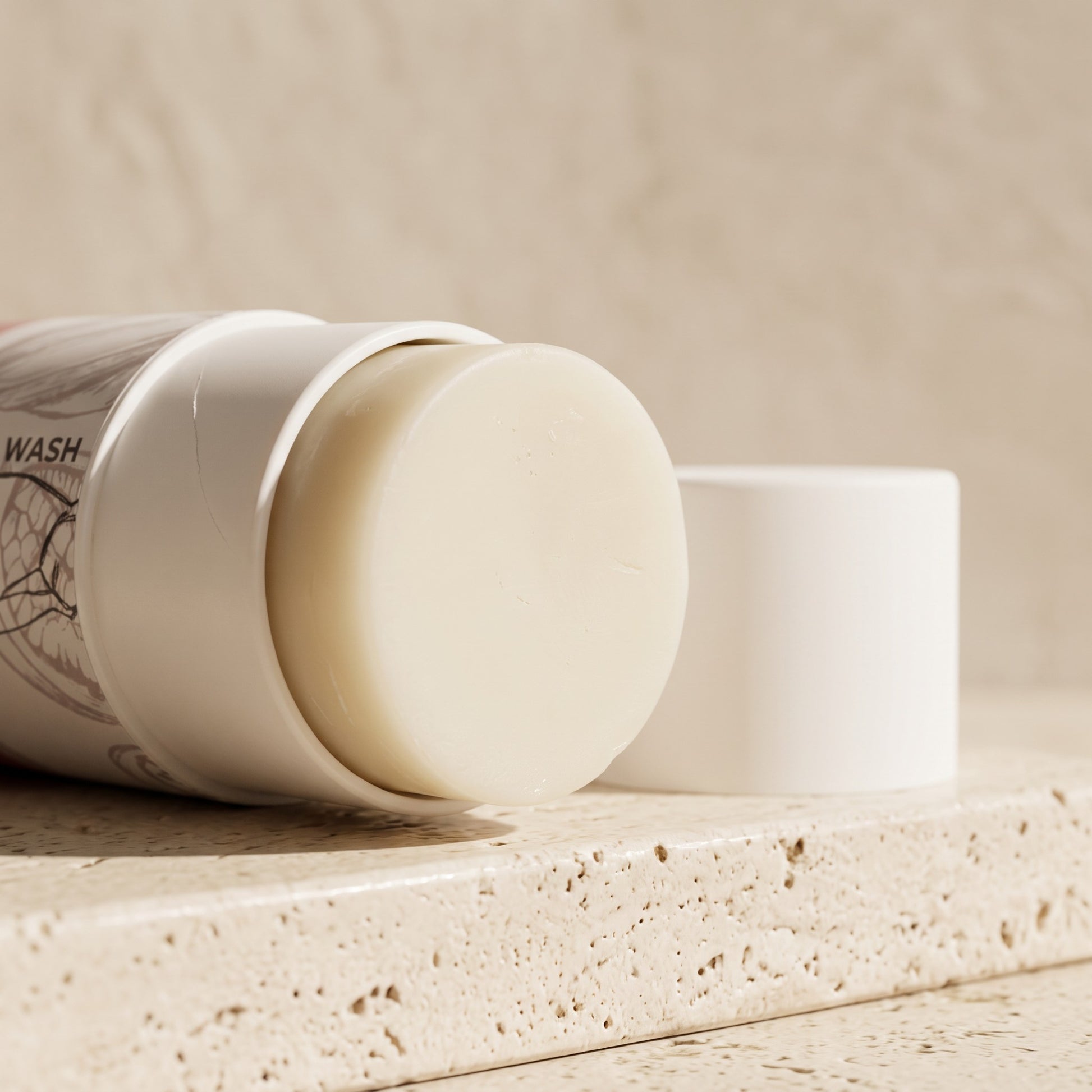 Pure Wash cocoa butter lotion bar in a white twist-up tube, resting on a textured stone surface.