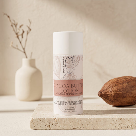 Pure Wash cocoa butter lotion stick in a white tube for dry skin, displayed on a stone surface with a cacao pod.