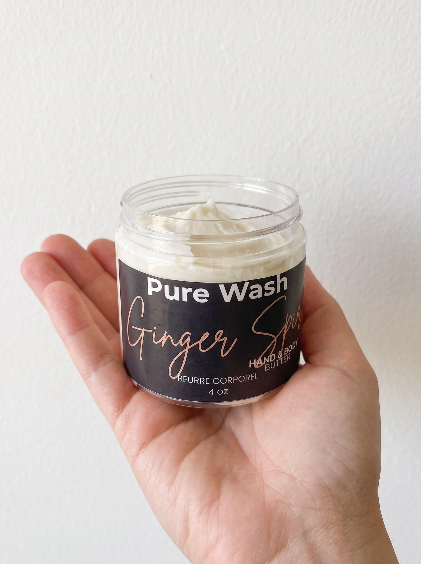 Pure Wash Ginger Spirit hand and body butter in a clear 4 oz jar held in a hand against a white background.