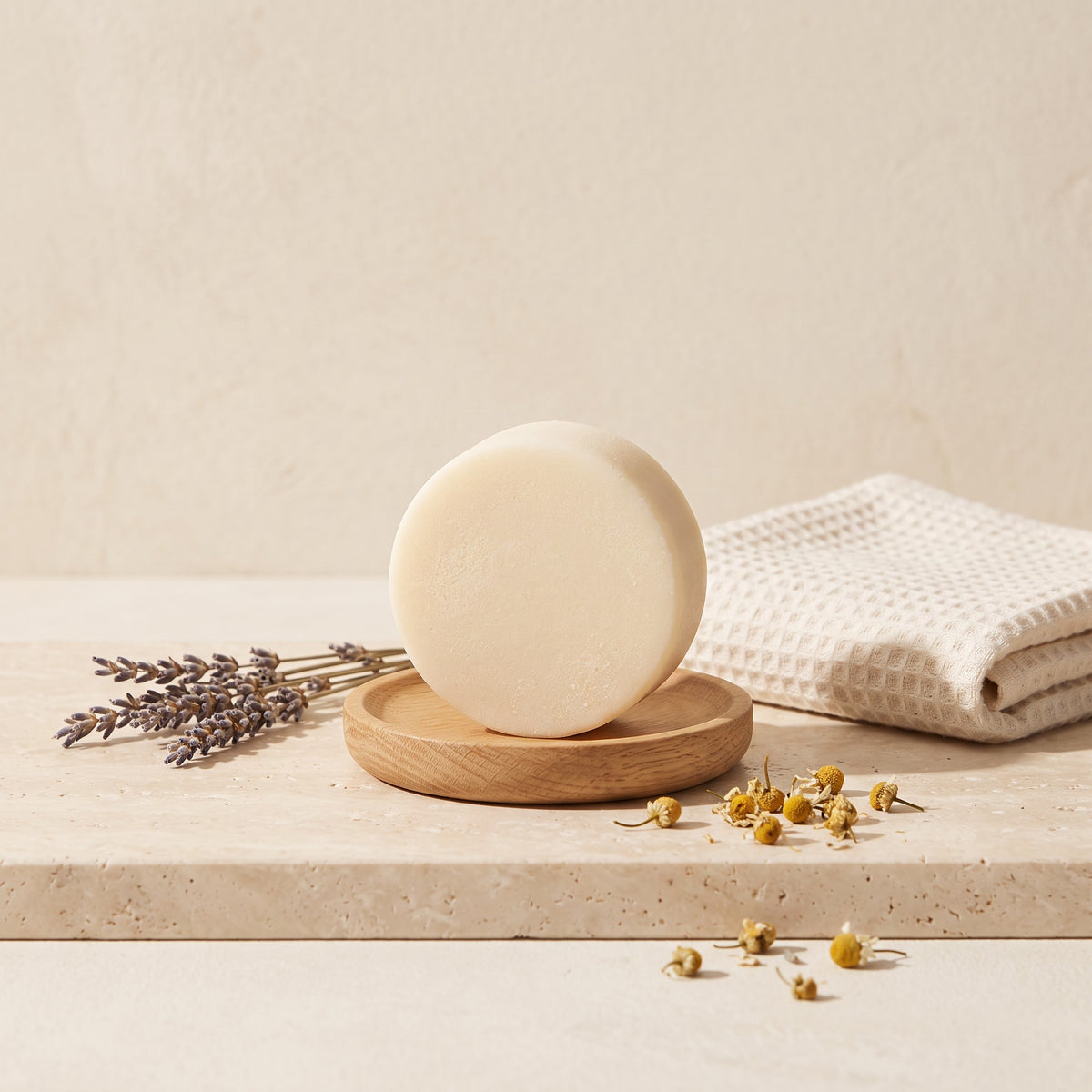 Pure Wash Lavender Chamomile conditioner bar on a wooden dish with dried lavender and chamomile flowers on stone.