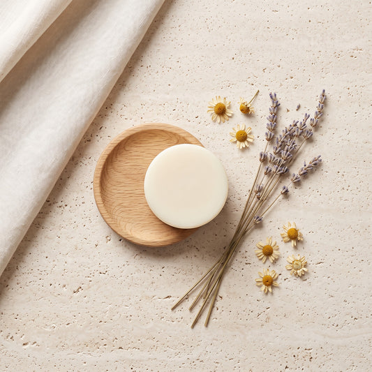 Pure Wash Lavender Chamomile conditioner bar on a wooden dish with dried lavender and chamomile flowers on stone.