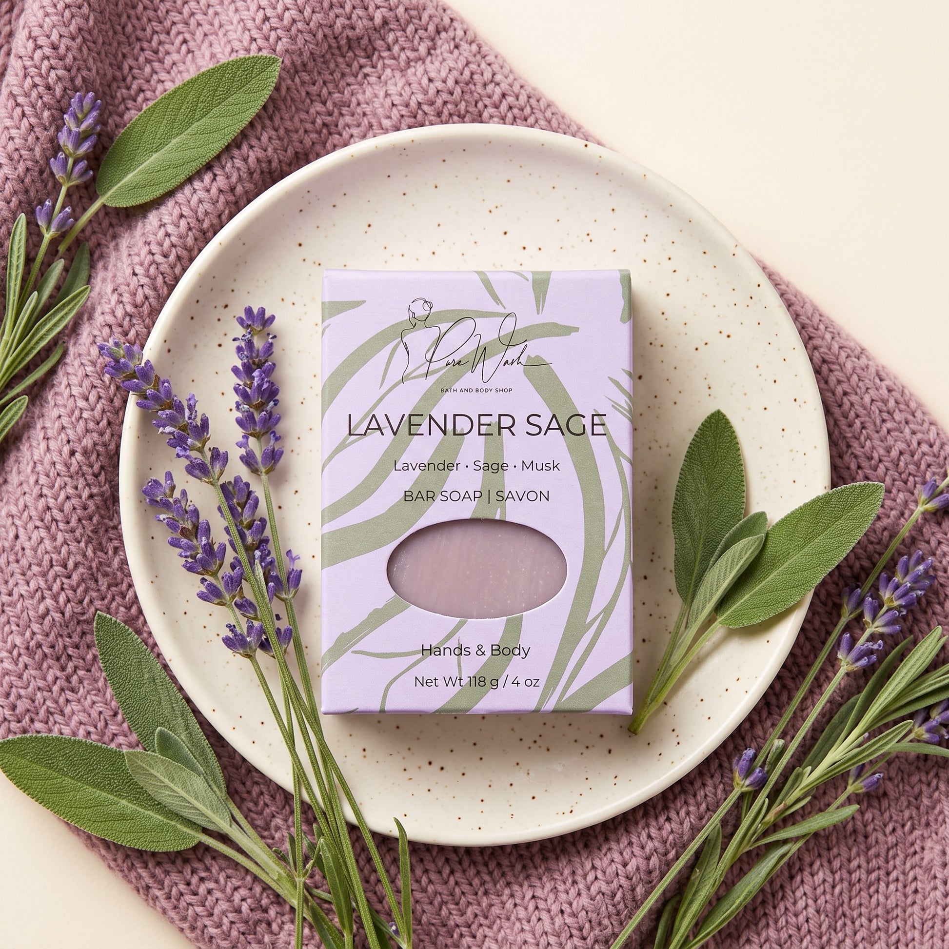 Pure Wash Lavender Sage soap bar in purple packaging on a speckled plate with fresh lavender sprigs and sage leaves.