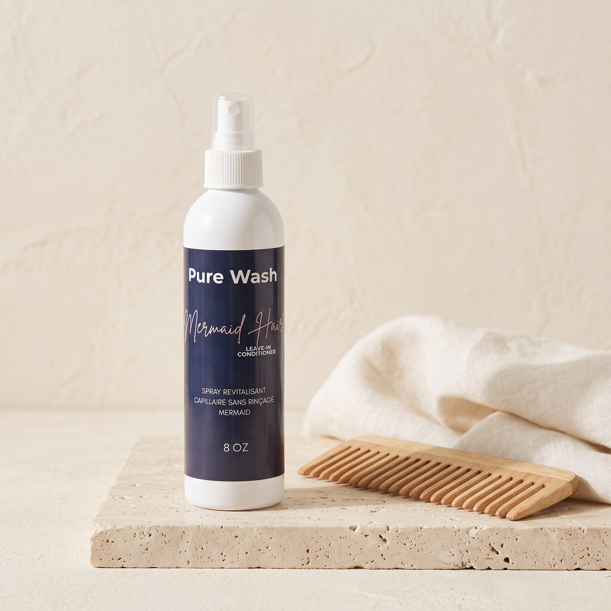 Pure Wash Mermaid Hair leave-in conditioner spray bottle with a wooden comb on a textured stone surface.