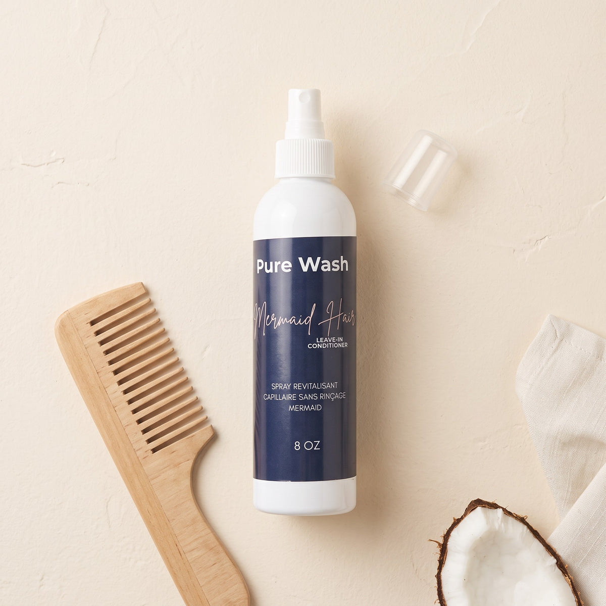 Pure Wash Mermaid Hair leave-in conditioner spray bottle with a wooden comb and coconut piece on a beige background.