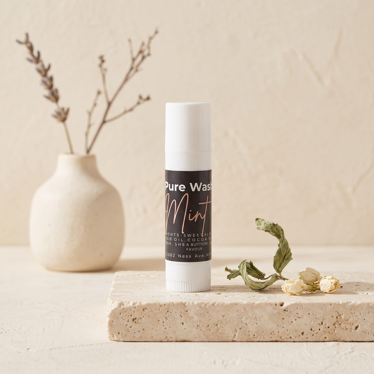 Pure Wash mint lip balm in a slim tube on a stone pedestal with dried flowers in a minimalist setting