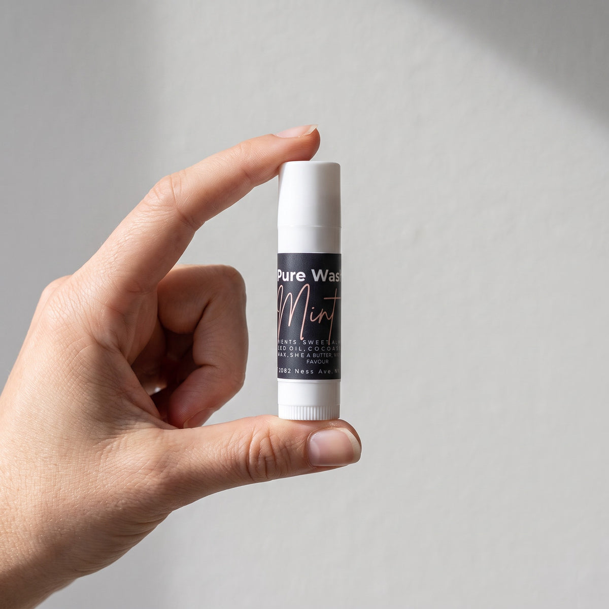 Pure Wash mint lip balm in a slim white tube held between fingers against a neutral background