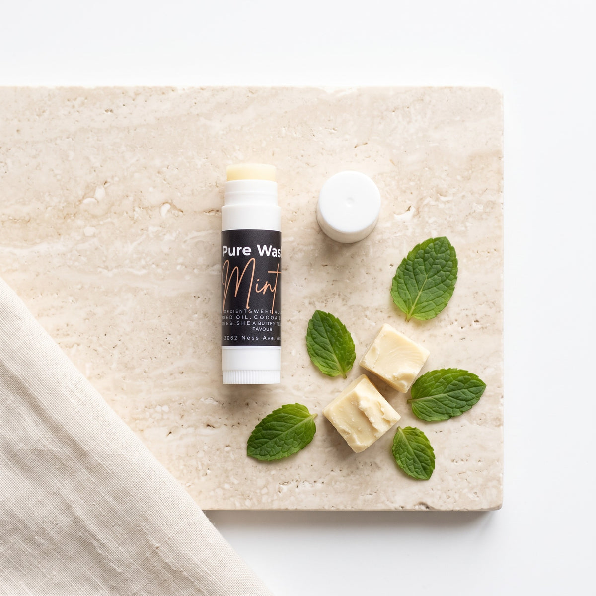 Pure Wash mint lip balm tube with beeswax and fresh mint leaves on a stone surface
