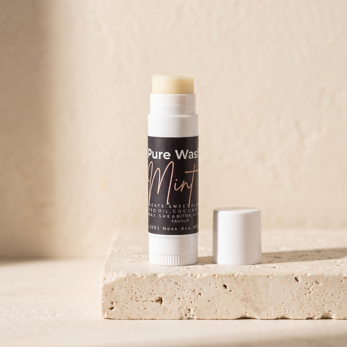 Pure Wash mint lip balm in a slim tube with beeswax, shea butter, and coconut oil on a textured stone surface.