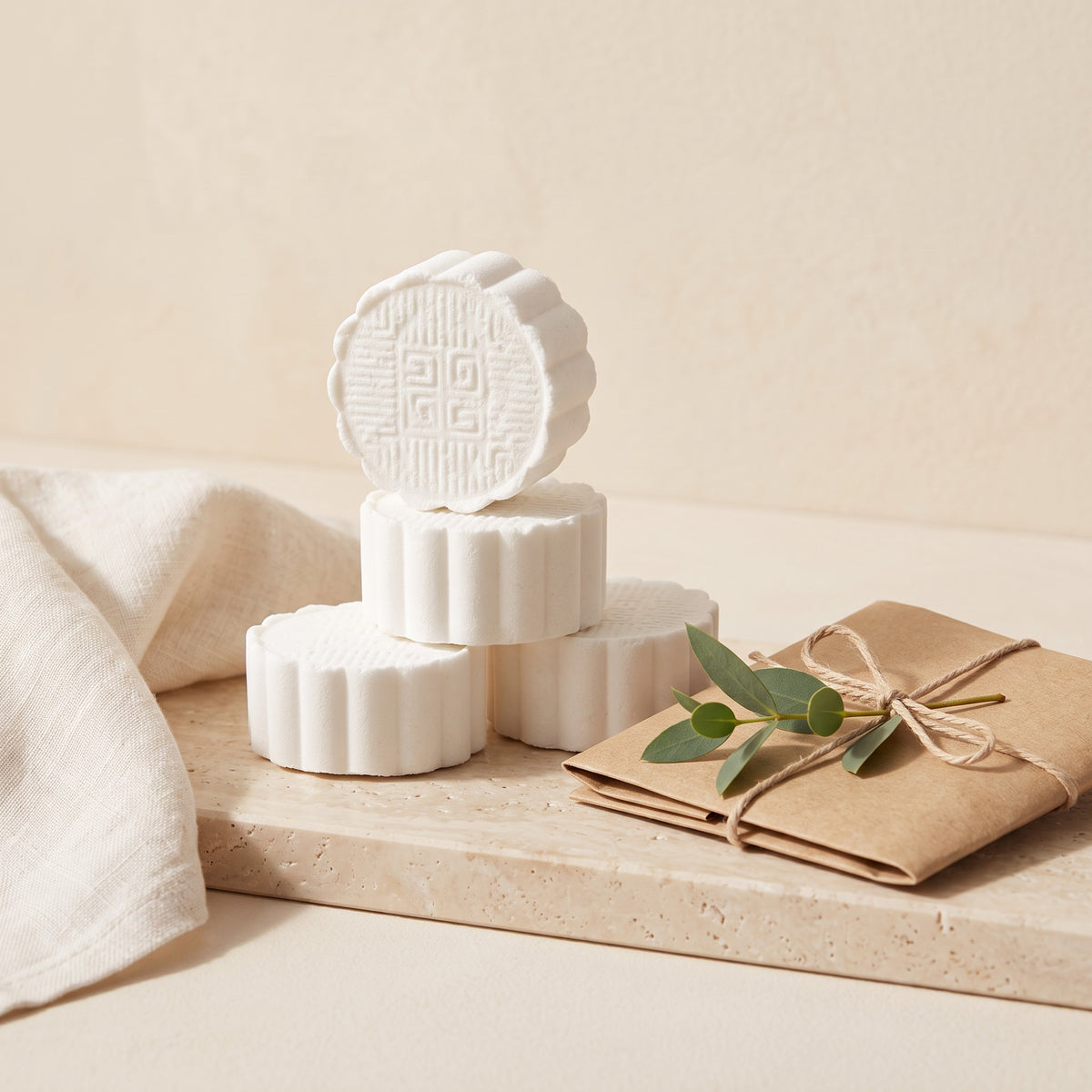 Pure Wash mint-scented shower steamers stacked on a stone tray with a wrapped gift and eucalyptus sprig.
