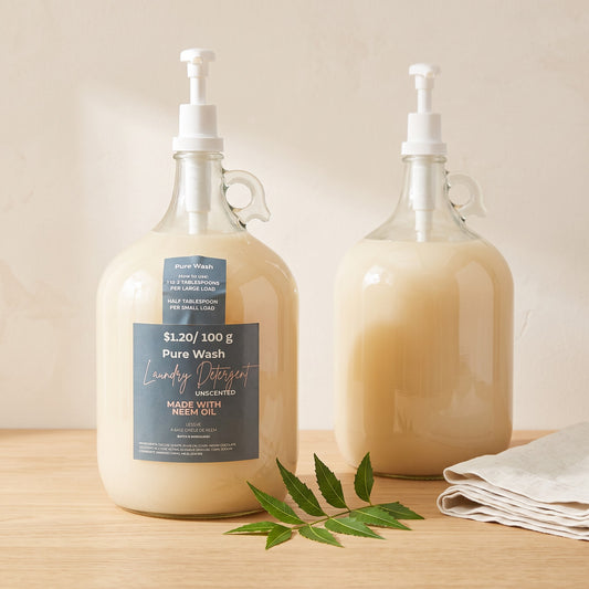 Pure Wash unscented laundry detergent in glass pump bottles with neem oil, displayed on a wooden surface.